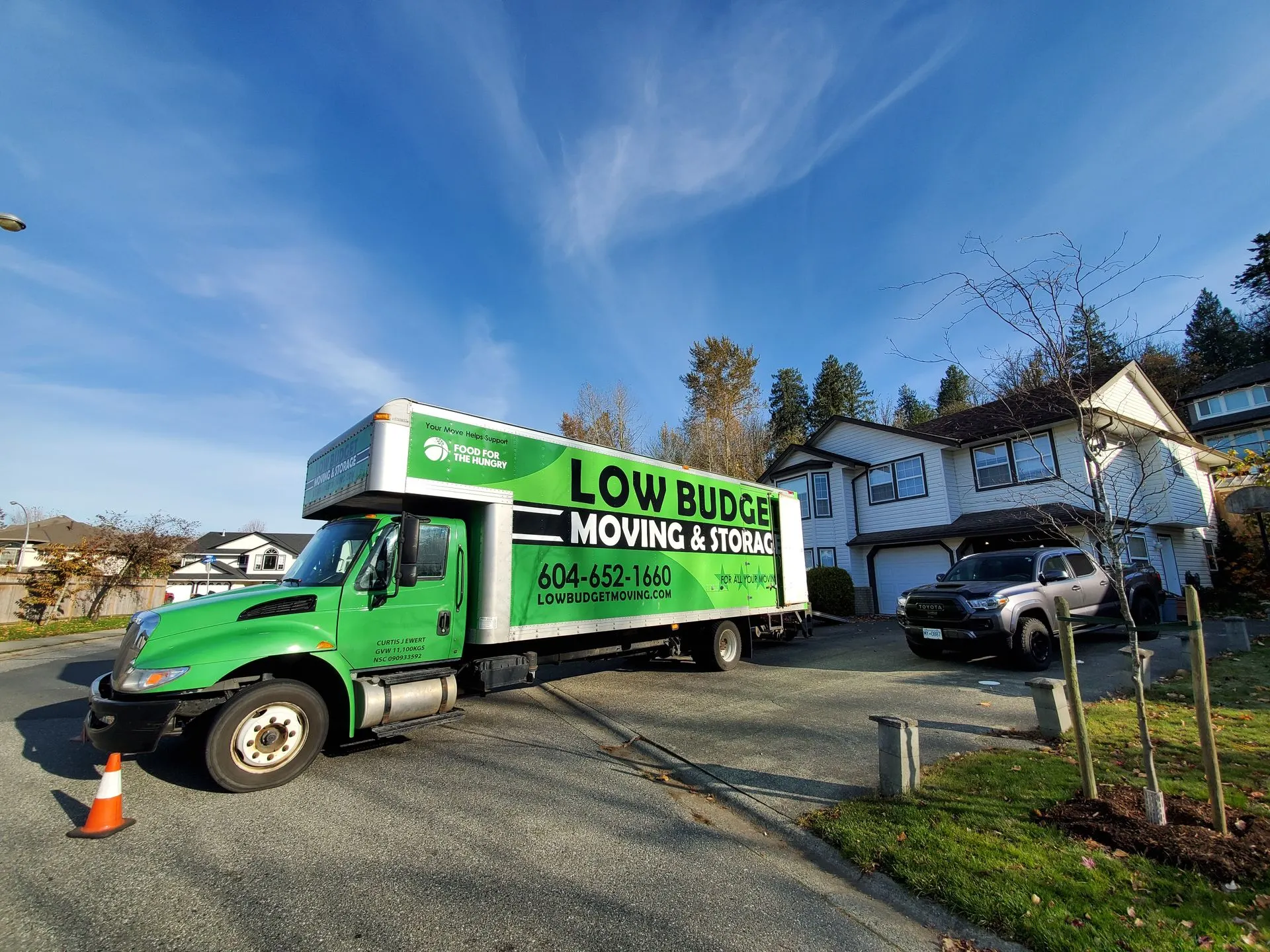 Low Budget Moving & Storage truck parked in front of a suburban house on a sunny day