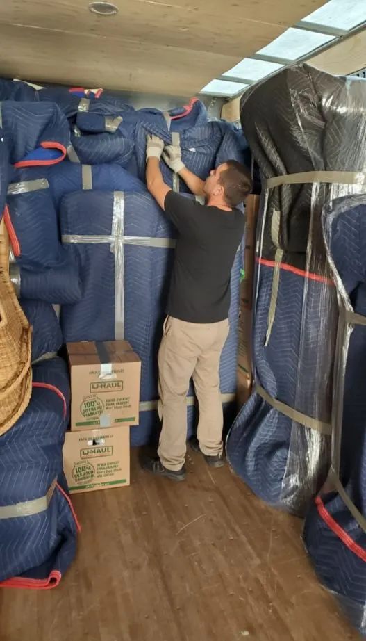 Mover arranging blanket-wrapped furniture inside a moving truck
