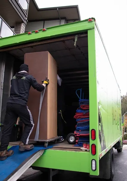 Mover rolling a tall box up the ramp into a green moving truck