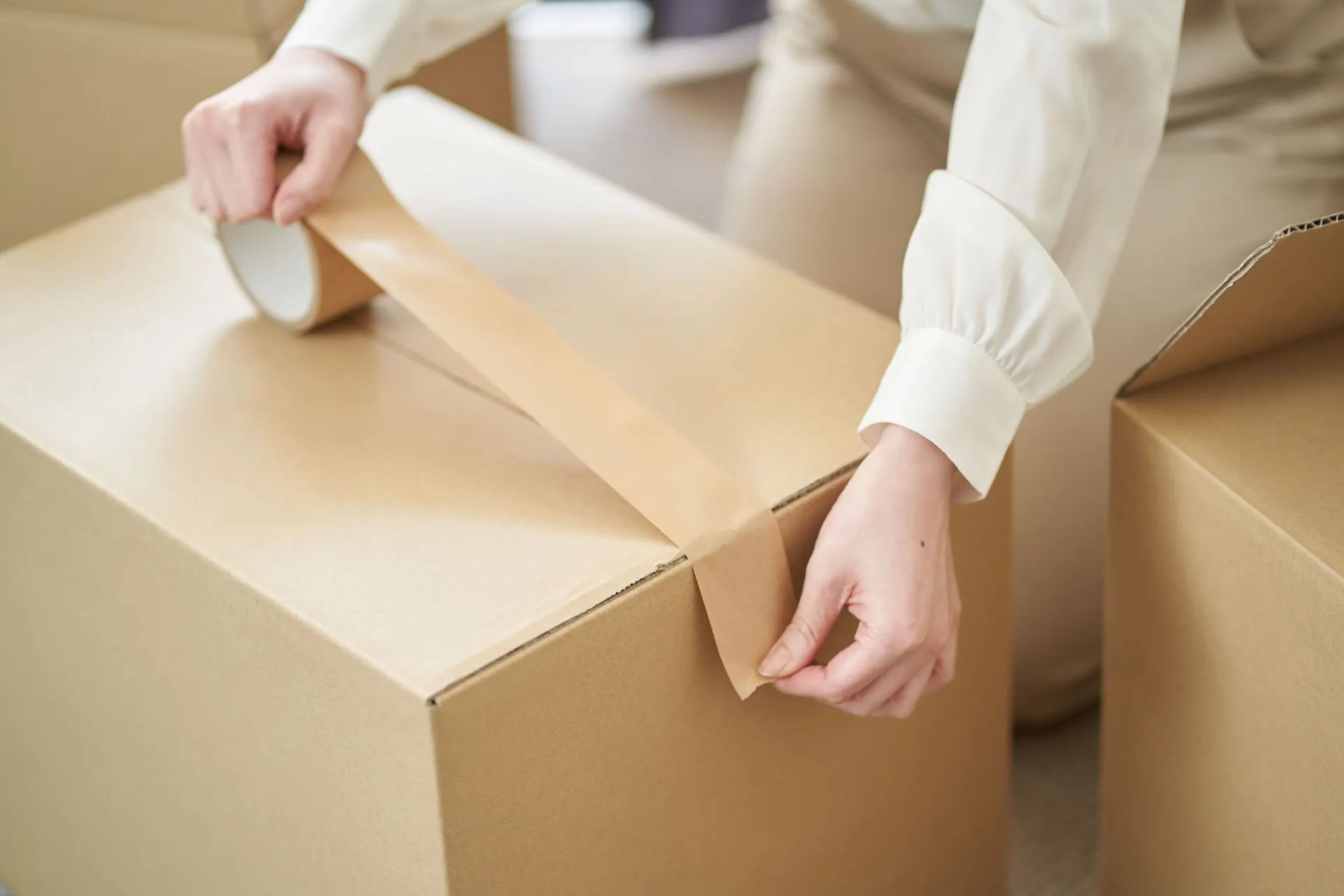 Hands sealing a cardboard moving box with packing tape