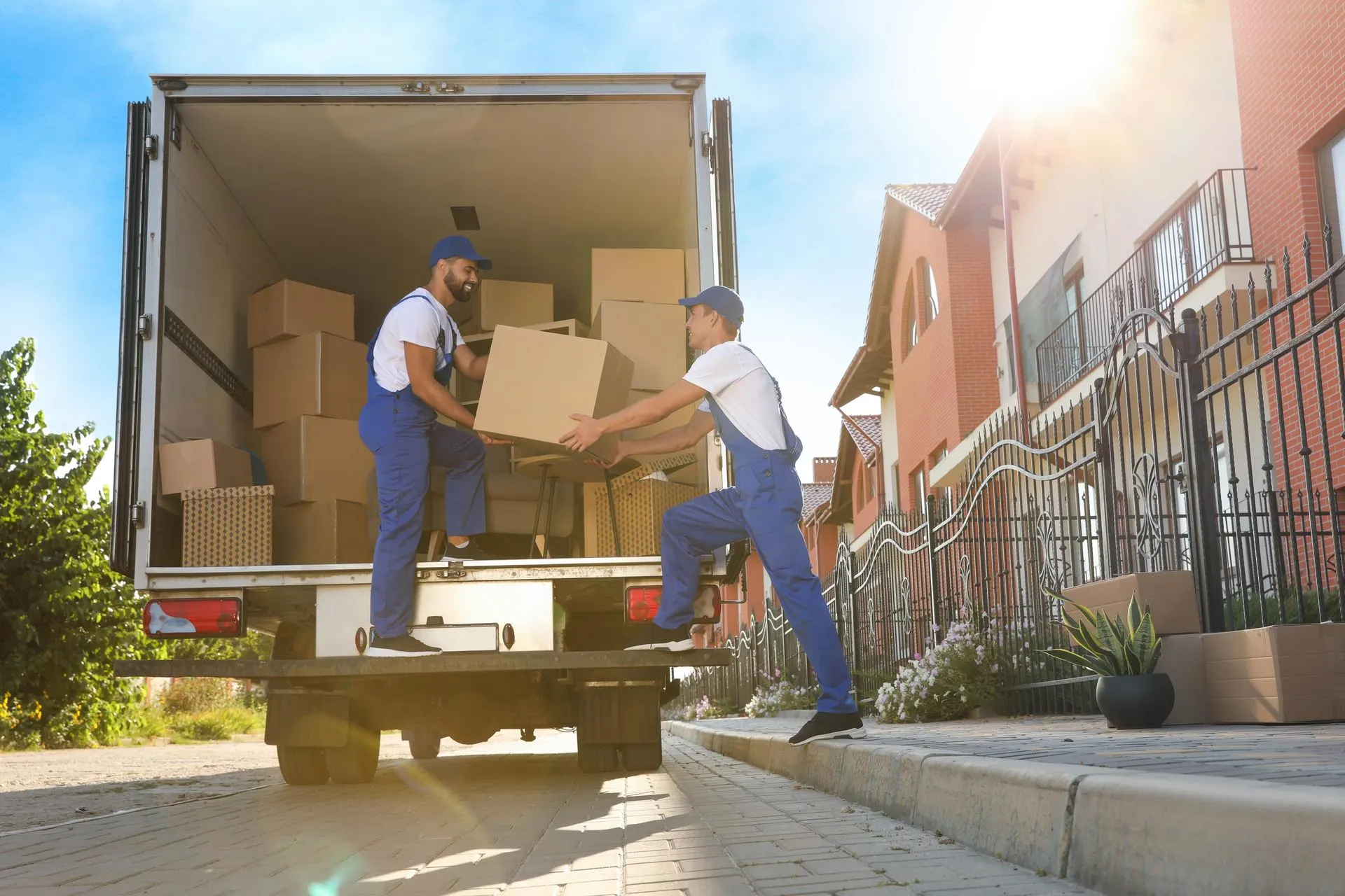 Two movers unloading boxes from a moving truck parked on a residential street