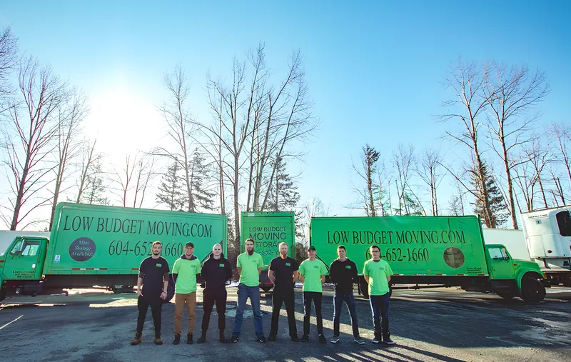 Low Budget Moving and Storage crew in green and black shirts lined up in front of their moving trucks